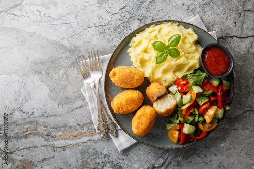 Hot chicken bechamel croquettes with mashed potatoes, vegetable salad and ketchup close-up in a plate on the table. Horizontal top view from above