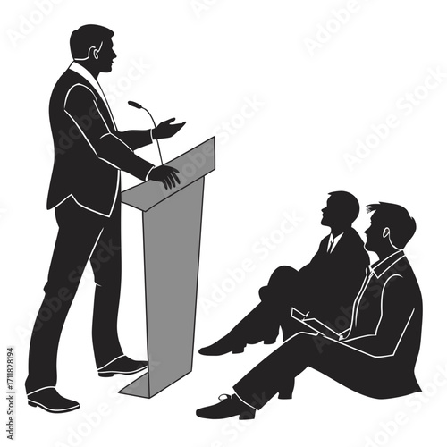 A man in a suit stands at a podium giving a speech to an audience seated on the floor.