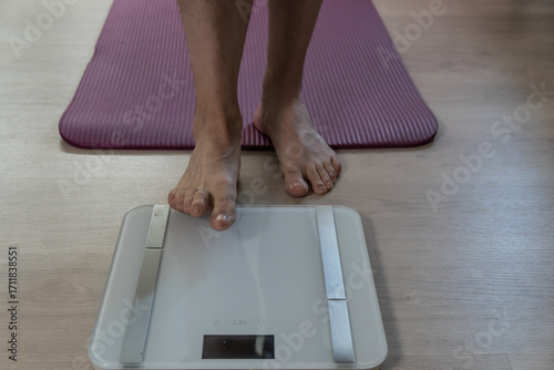 Man checking weight on digital scale for health monitoring.  Close-up of male feet on a modern digital scale placed next to a yoga mat at home. Concept of personal health tracking, body weight control