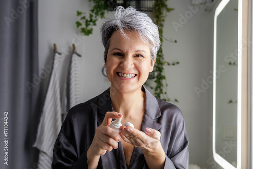 Mature beautiful woman during menopause with gray hair applies hormonal anti-aging cream
