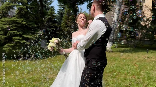 A beautiful wedding video. The happy newlyweds take photos in a park with soap bubbles.