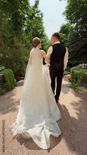 A beautiful wedding video. Happy newlyweds walk along a road in a park.