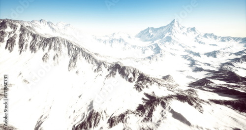 Vast mountain range stretches across the horizon, adorned with a thick blanket of snow. The bright blue sky enhances the serene winter landscape, creating a captivating natural beauty.