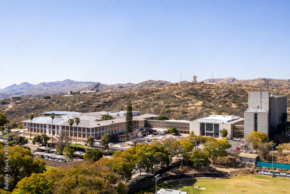 Naklejka premium Downtown Windhoek, Namibia, with tall contemporary buildings, wide streeodern ts, moving cars, and a clear blue sky.