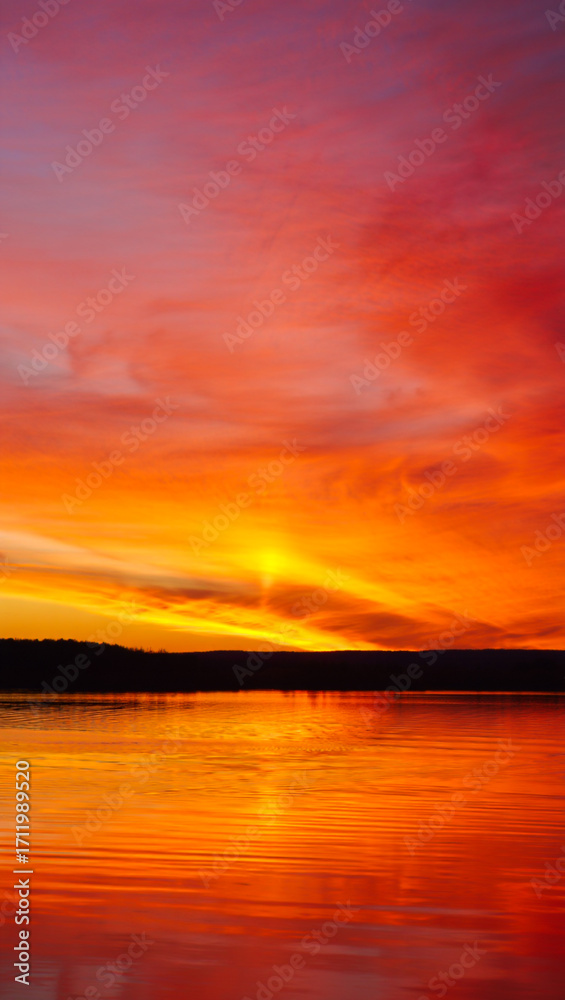 Obraz premium Vibrant sunset over calm water reflecting fiery sky colors