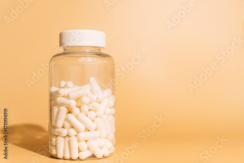 Clear bottle with white capsules on beige background. High quality photo