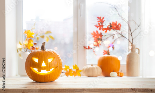 Orange jack o lantern pumpkin on wooden table with copy space over blurred window sill background with traditional Halloween house decoration