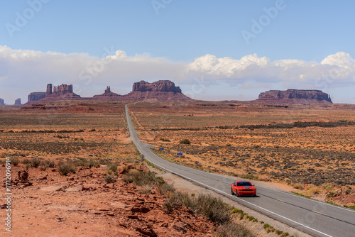 Red car driving on long straight road at Forest Gump point at Monument Valley USA, road trip concept