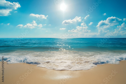 Soft waves roll onto a sunlit beach while fluffy clouds drift in the blue sky on a warm afternoon by the ocean