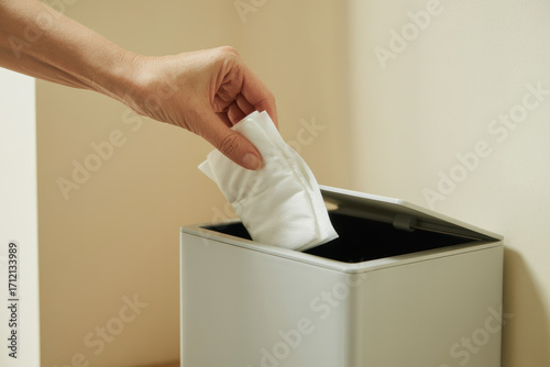 Hand disposing sanitary pad in small bin against beige wall background for personal hygiene and safe feminine care practices