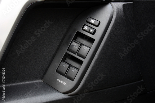 Close-up of black car door panel with power window control buttons, lock switches and textured surface, showing modern automotive interior design and functionality.