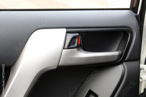 Close-up of a car interior door handle in silver metallic with black textured plastic and a small red safety accent, showcasing modern ergonomic design and durable materials.