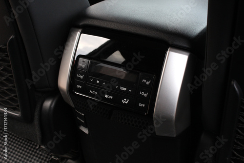 Rear passenger car climate control panel with digital display, black buttons, silver trim, and seat heating switches, integrated in leather back console.