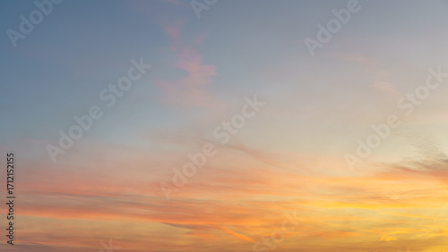 Soft orange and pink clouds drift across a pale blue evening sky