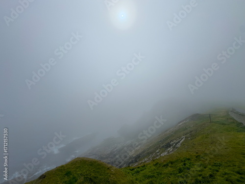 Dramatic seascape coastal view with thick sea mist and sun with halo  attempting to breakthrough clouds. Sumburgh Head. Shetland