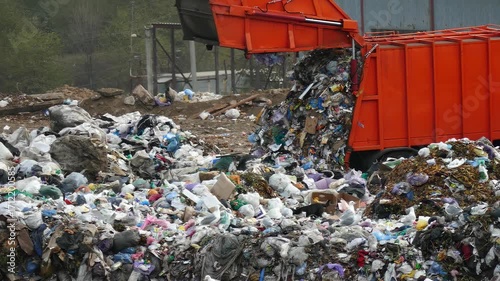 Garbage truck dumps trash at the city landfill. A pile of garbage smokes from waste decomposition. An environmental disaster caused by improper waste disposal.
