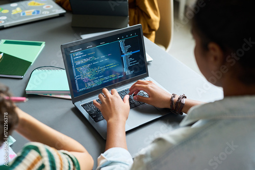 Quadro su tela Teenage Black girl coding on laptop, sitting at desk with hands on keyboard, foc