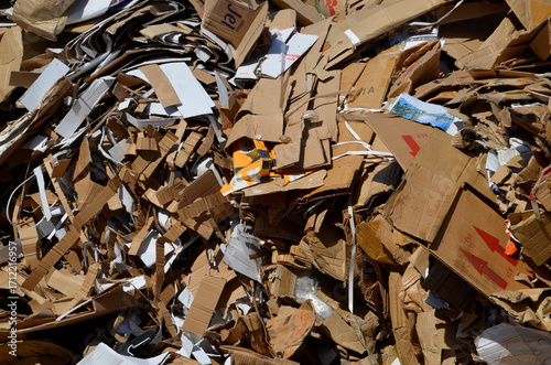 A large, dense pile of flattened cardboard boxes and paper waste collected separately for recycling. The image represents modern efforts towards sustainability.