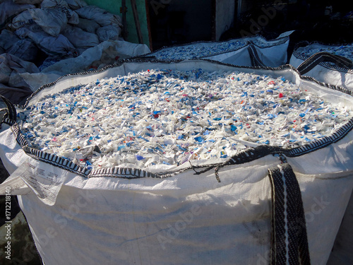 Close-up of shredded, multicolored polyethylene terephthalate (PET) plastic flakes and pellets, derived from recycled bottles, filling a large industrial bag at a material recovery facility.