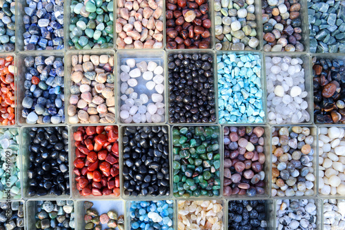 Top view of colorful tumbled gemstones sorted in small boxes. Ideal for themes of minerals, jewelry craft, retail display, crystal collection, healing energy, color background.