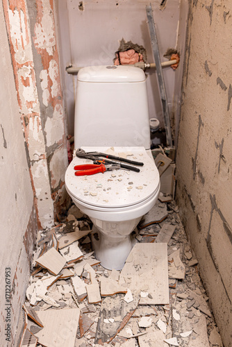 A toilet renovation, with broken tiles and a pile of debris in the middle of the toilet with tools