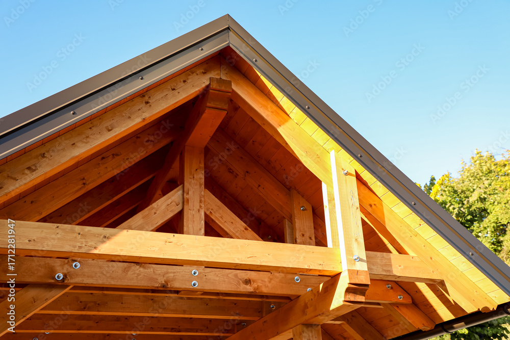 Obraz premium Sunlight gently filters through a beautifully constructed wooden roof framework, revealing exposed beams and strong bolts that emphasize the rich grain of natural wood.