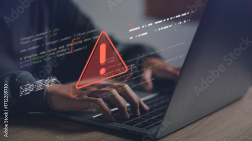 Close-up of hands typing on laptop with warning error icon and code overlay, representing data error, system failure, cybersecurity issues, and digital troubleshooting in modern technology.
