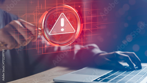 Businessman using laptop with magnifying glass highlighting digital warning icon, symbolizing digital risk, cybersecurity threats, data protection, and online risk management in modern technology.