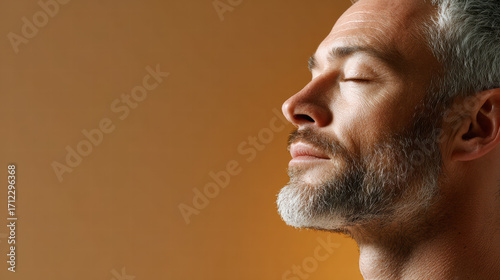 Relaxed bearded man profile with closed eyes enjoying calm moment in warm studio light, neutral background, soft texture, peaceful expression, contemplative mood