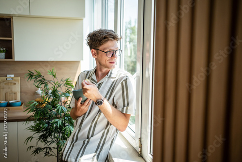 Картината върху платно Young man enjoying morning breakfast by kitchen window