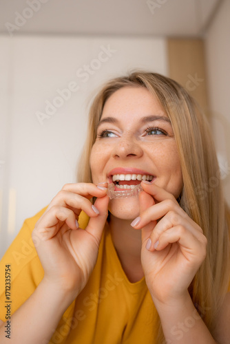 Woman smiling while inserting clear dental aligner into her mouth