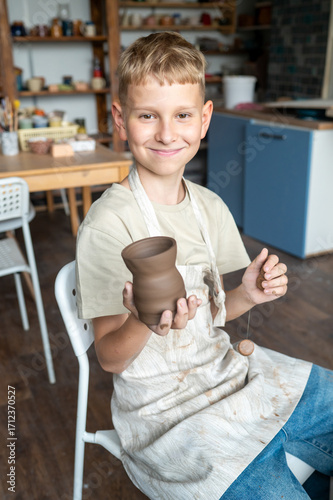 Young boy smiling with freshly made clay cup in workshop