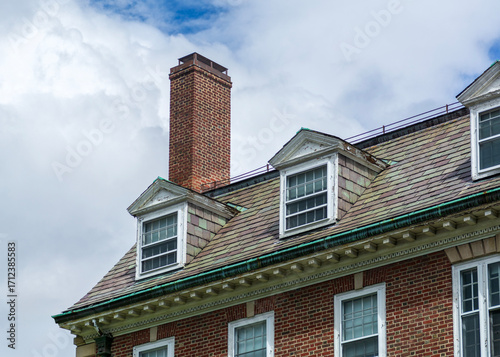 Historic brick building with dormer windows and slate roof under cloudy sky in Cambridge, Massachusetts, USA