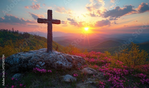 A stone cross atop a mountain at sunset, surrounded by blossoming pink flowers