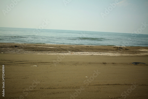 Cuadro en lienzo An empty sandy beach with soft waves rolling onto the shore under clear daylight