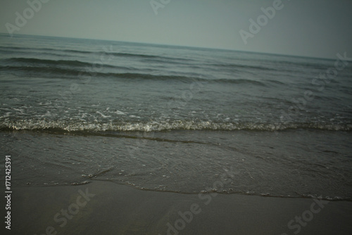 Bild auf Leinwand Minimalist seascape with a gentle wave washing over wet sand in the shallows