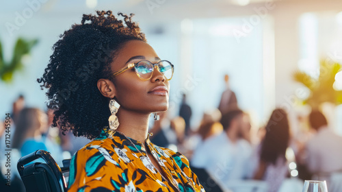 Thoughtful Black woman with curly hair and stylish glasses looking up attentively in bright, modern professional conference or event setting
