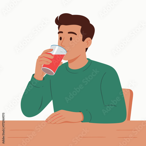Young man in a green sweater sitting at a table and drinking red juice from a glass.