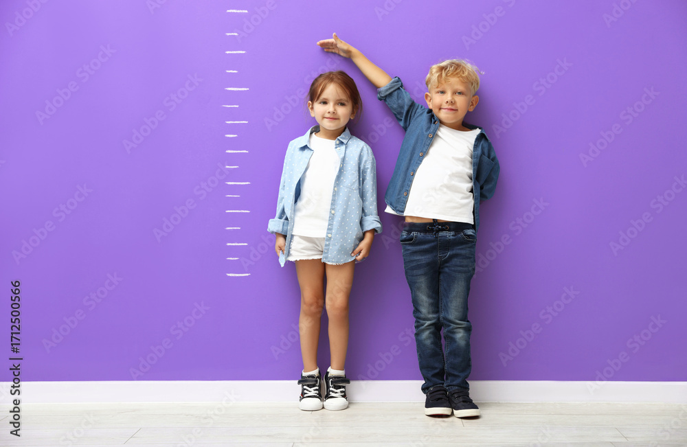 Obraz premium Cute little girl and boy measuring their heights near violet wall with scale