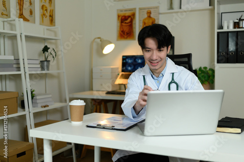 Wallpaper Mural A cheerful young male doctor consults a patient via laptop in a modern clinic with anatomical posters and medical tools Torontodigital.ca