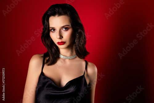Beautiful young woman with stylish black dress posing against a dramatic red background