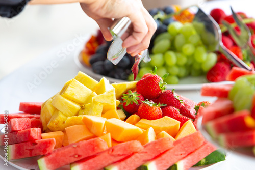 Caterer serving strawberries on fresh fruit platter at buffet table