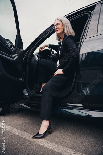 Fototapeta Successful mature businesswoman stepping out of a car in an elegant outfit on an