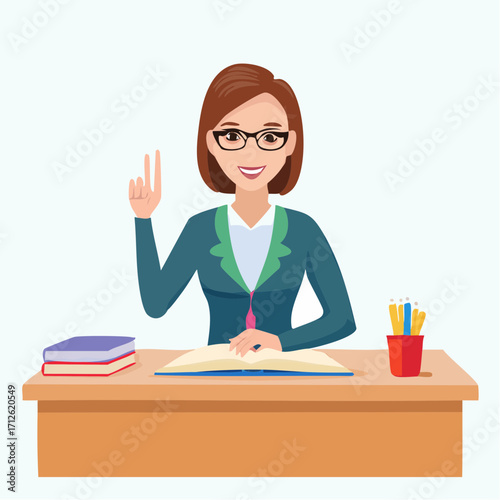 A smiling female teacher wearing glasses is sitting at a desk with an open book and two fingers raised