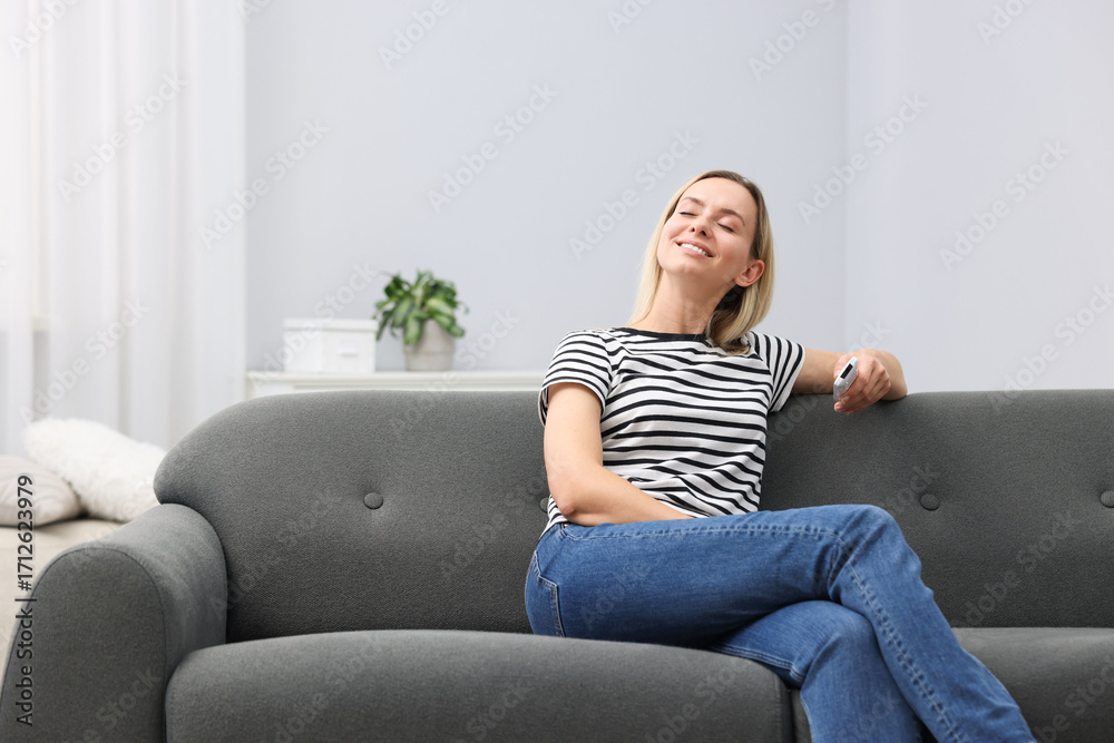 Obraz premium Woman with air conditioner remote control on sofa at home. Space for text