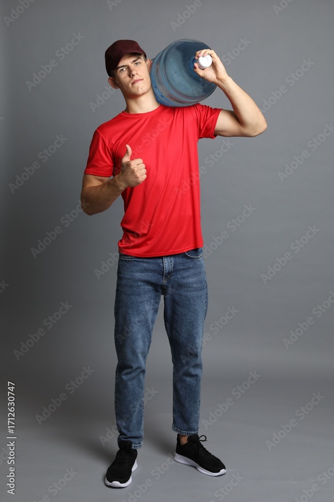 Naklejka premium Delivery man with cooler bottle of water showing thumbs up on grey background