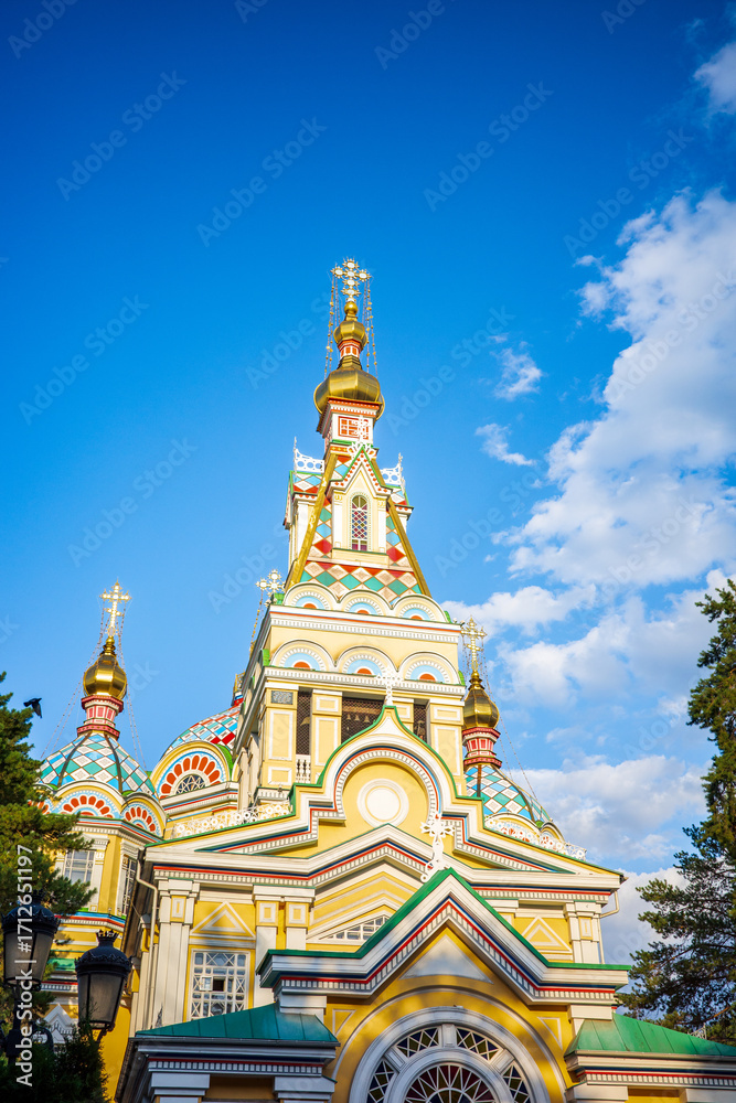 Fototapeta premium Close-up of the golden domes of Zenkov Cathedral in Almaty, Kazakhstan. With its vibrant painted details, ornate Orthodox design, and striking contrast against the blue sky of the iconic wooden church