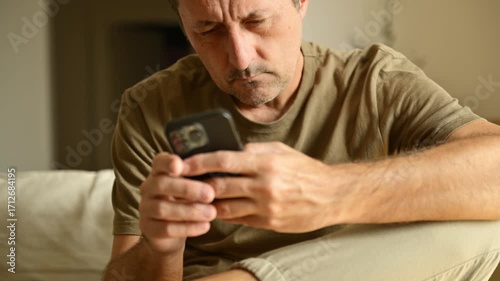 Stressed man holding his head while looking at smartphone, frustrated and worried expression indoors. 4k.
