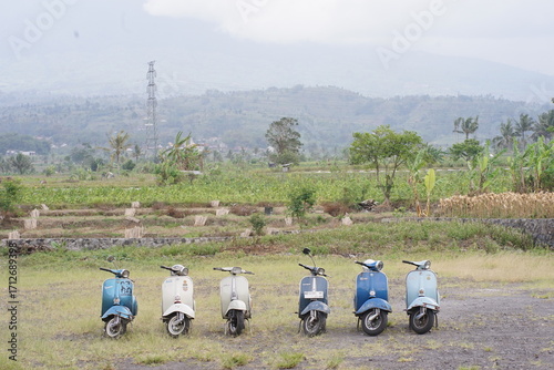 Vintage scooters parked on a lush green field with mountain backdrop