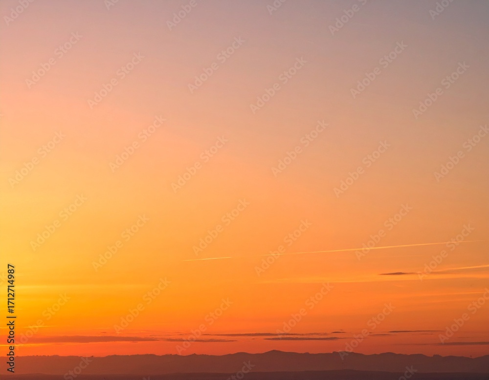Fototapeta premium Vibrant orange and yellow gradient sky at sunset with a distant dark horizon line.
